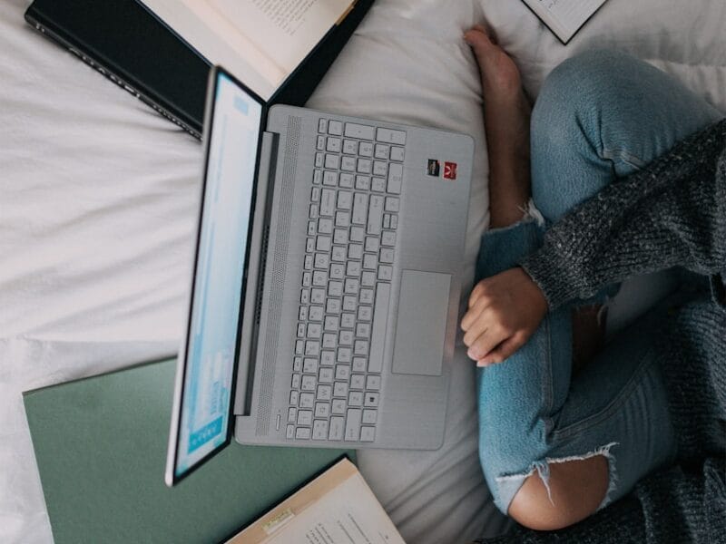 woman in blue long sleeve shirt and blue denim jeans sitting on bed using laptop
